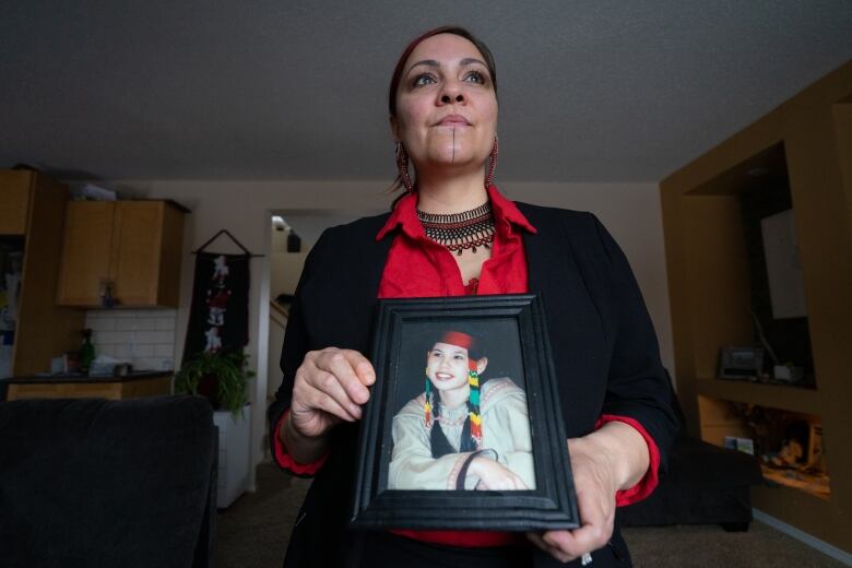 A woman stands holding a portrait of a young woman.