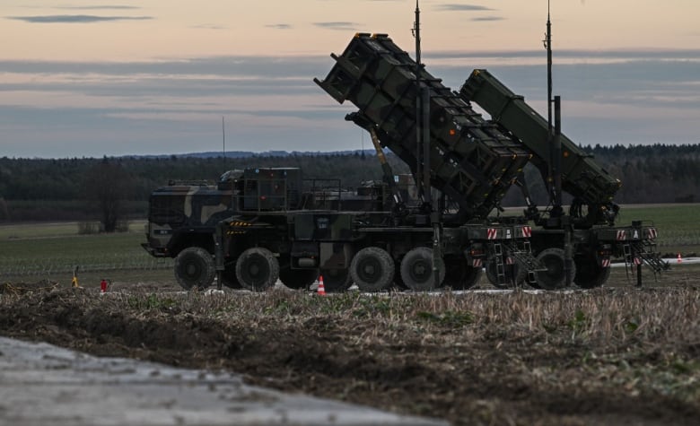 A large, dark green missile launcher tilted upward on the back of a military vehicle parked in a field. 