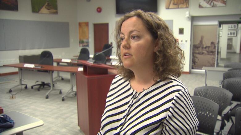 Mayor Rebecca Alty stands in City Hall chambers wearing a striped shirt.