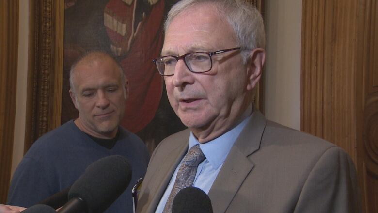 A man in a suit and glasses speaking into a microphone.