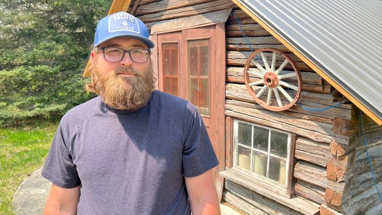 A man in a baseball cap standing in front of a vintage barn.