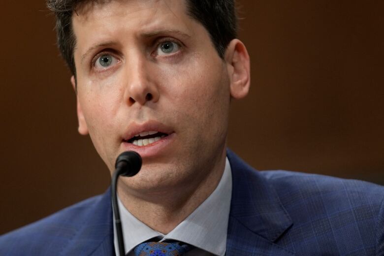 A man in a jacket and tie speaks into a microphone