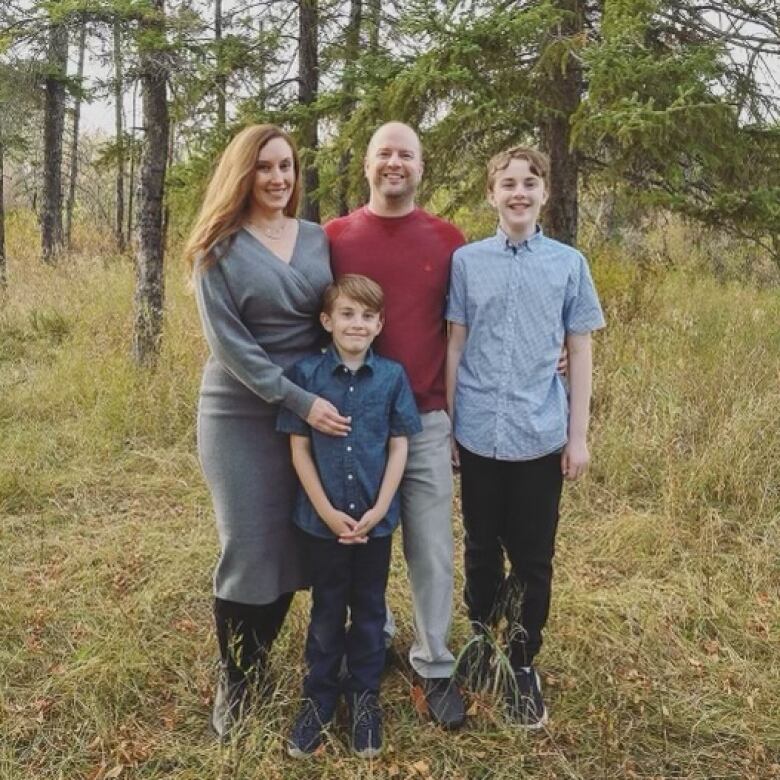 A family is standing with trees in the background. Father, mother and two sons can be seen. 