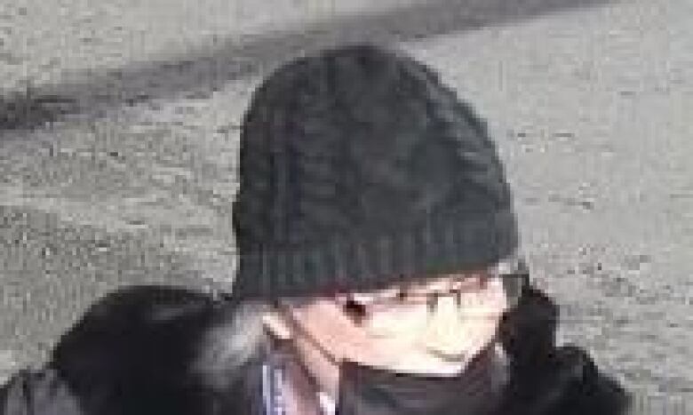 A close-up, blurry photo of a middle-aged woman wearing a black toque, glasses and surgical mask.