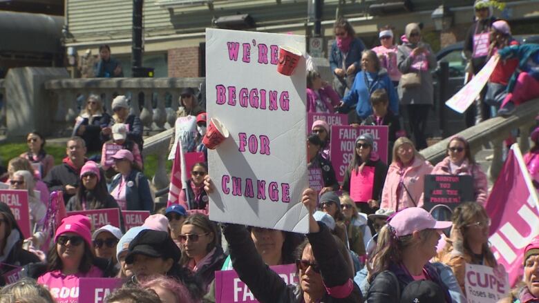 A woman holds up a sign that says, 