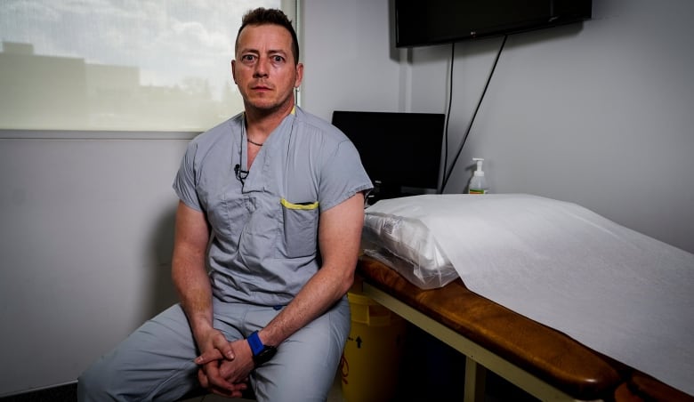 A doctor wearing scrubs sits in an examination room.