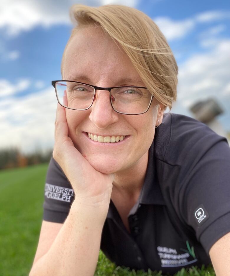 A woman with short hair lying on the grass with her hand on her chin