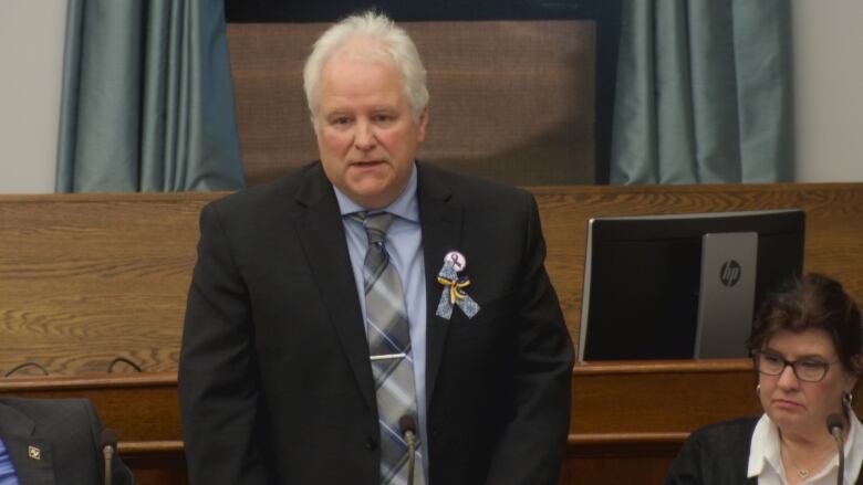 A man stands in the P.E.I. legislature wearing a suit.