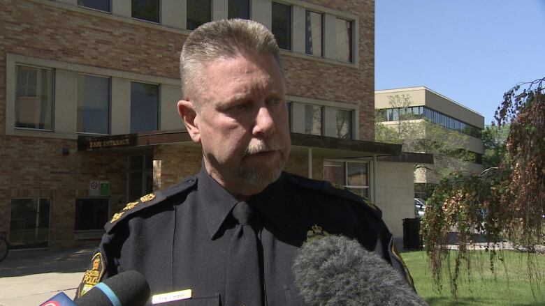 A police chief in his uniform can be seen talking to the media outside a building. 