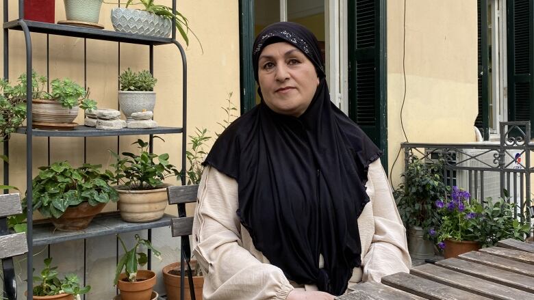 A woman wearing a head scarf sits at a table on an outside terrace.