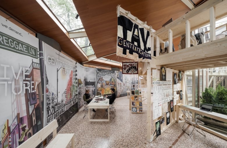 Two people sit at a table inside a pavilion covered in posters.