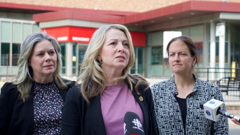 Three women stand in front of microphone. 