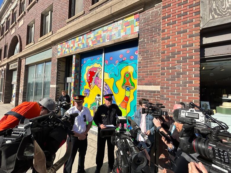 Two uniformed police officers are surrounded by media holding cameras and microphones.