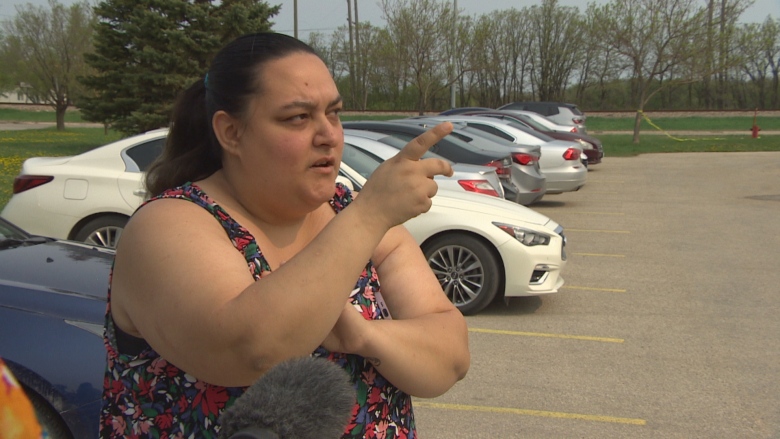 A woman stands being interviewed by media and points at where she used to live. 