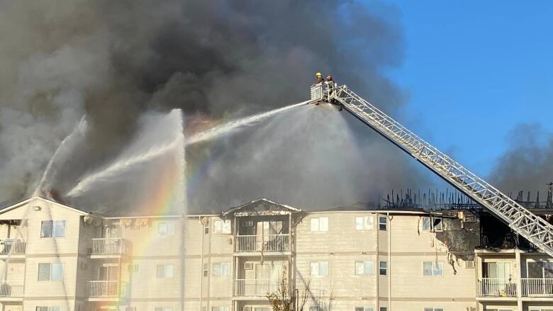 fire fighters use a bucket and ladder to spray water on a burning building. 