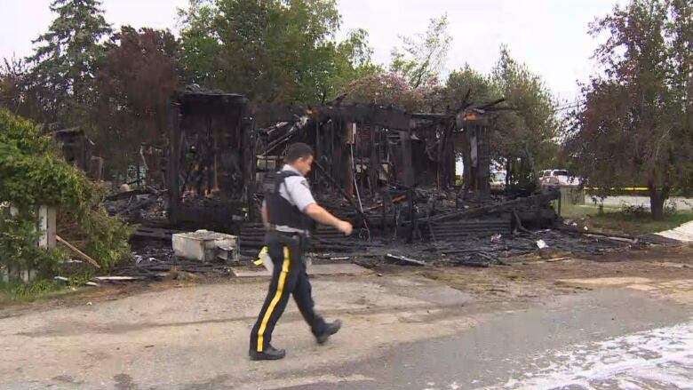 A uniformed police officer walks past the charred remains of a building.