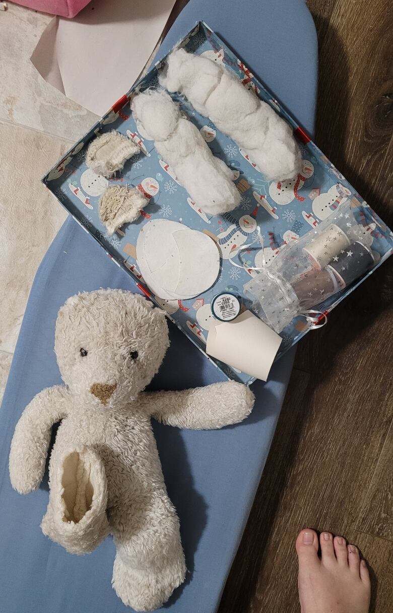 A stuffed animal with no ears or feet sits next to a tray of fabric, stuffing and sewing supplies.