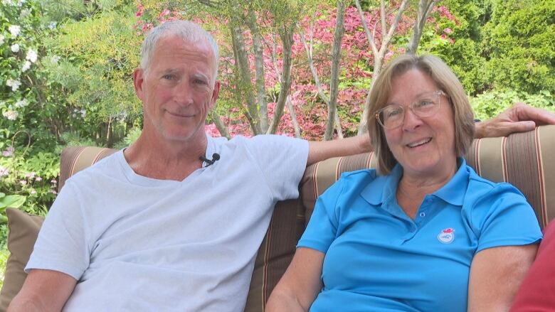 A man and woman sit beside each other outside, smiling.