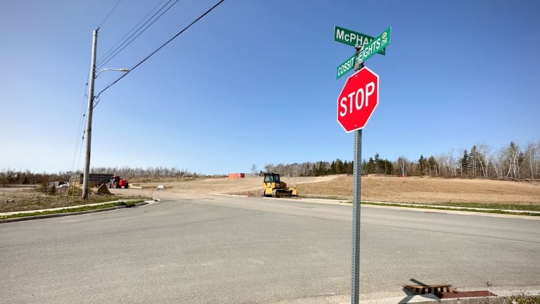 A stop sign at a street intersection in the foreground with an empty lot behind it and some cohnstruction equipment sitting idle.