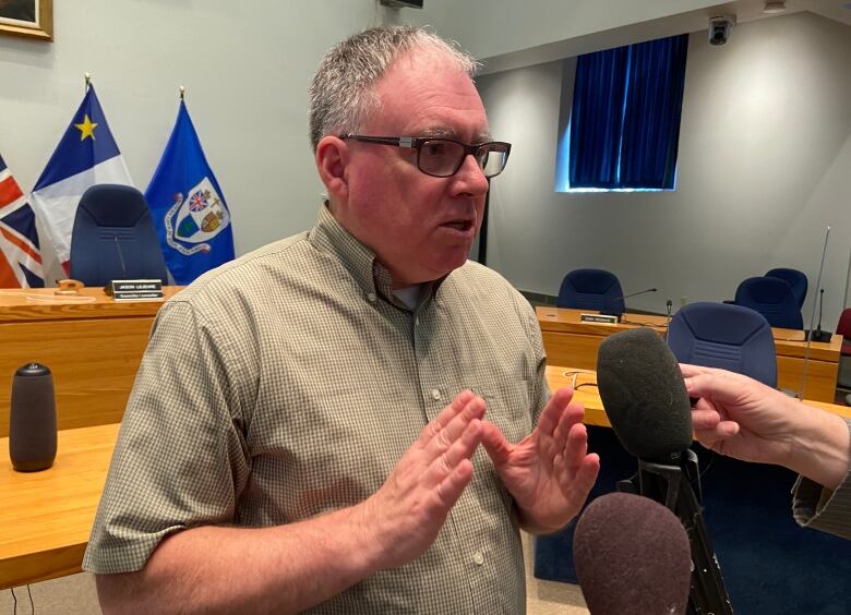 A man speaks into microphones while standing in Fredericton city council chambers.