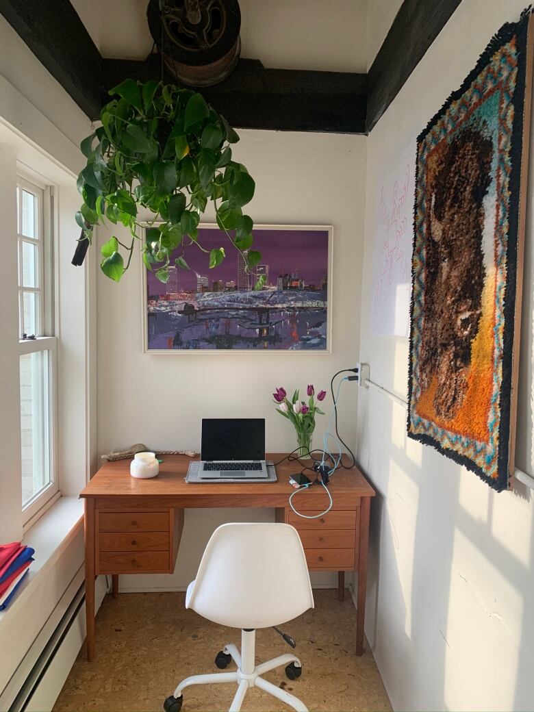 A narrow space with a desk against a wall and with art hung on the walls and a white desk chair