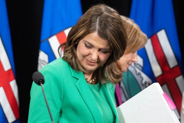 A politician wearing green looks downwards as she walks away, binder in arm.