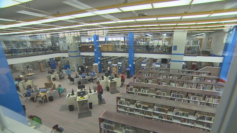 Inside regina public library central location from the second floor looking down on people at computer terminals and scanning aisles of books.