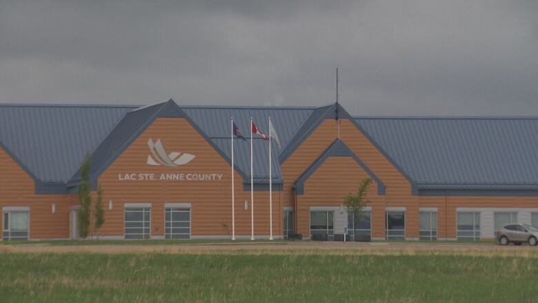 An orange and blue building is seen on a cloudy day with three flags blowing in the wind.