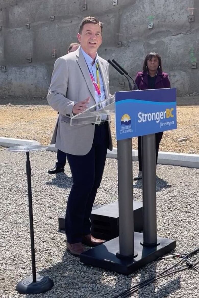 A man in a suit and tie speaks from behind a podium in an outdoor setting.