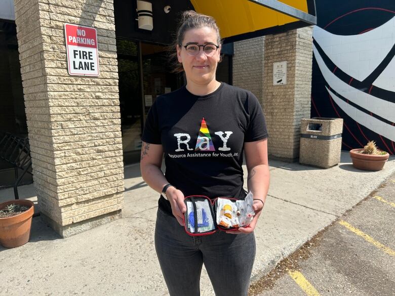 A woman wearing a black shirt that says RaY holds a kit filled with vials and needles. 