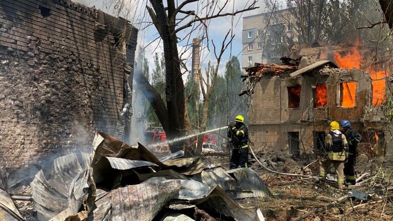 A firefighter sprays water on the ground amid wreckage in front of a destroyed building.