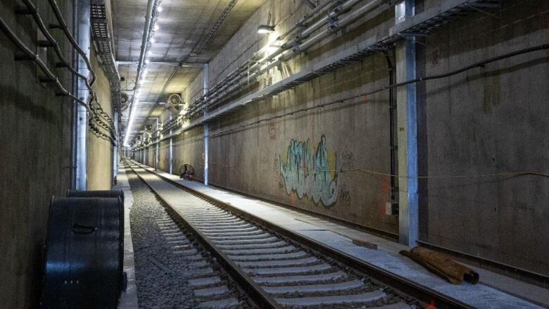 Tracks run through a tunnel, which has graffiti on one wall