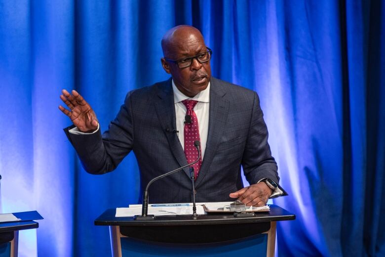 Man wearing a blue suit gestures as he speaks at a podium.