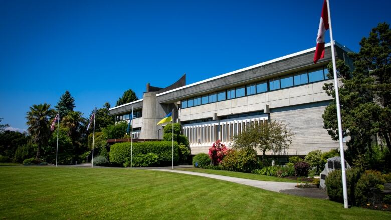 A concrete government building is pictured on a sunny day. A well-maintained lawn is pictured, as are Canadian and Ukranian flags.