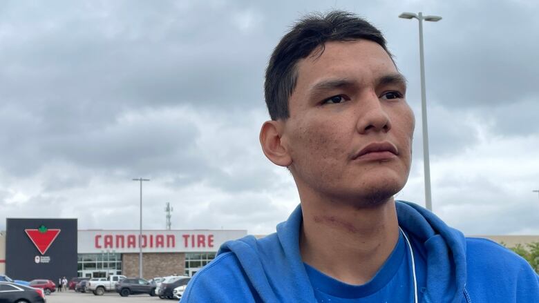 A man in a blue sweater stands outside a Canadian Tire store