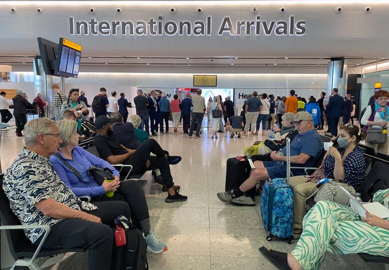 People sit and stand in a crowded airport.