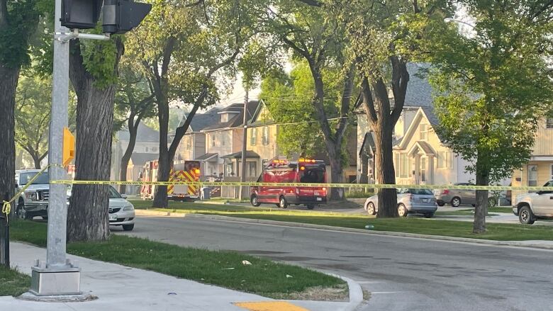 Fire trucks are parked outside a home on a street and yellow police tape is blocking people from getting near it. 