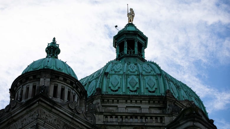 The exterior of a legislature building with blue domes and a golden statue.