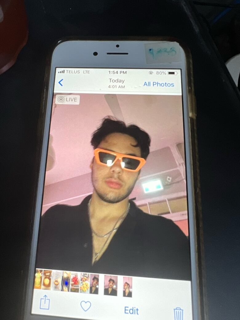 An iPhone is pictured with a photo of a man wearing bright orange sunglasses pulled up. 