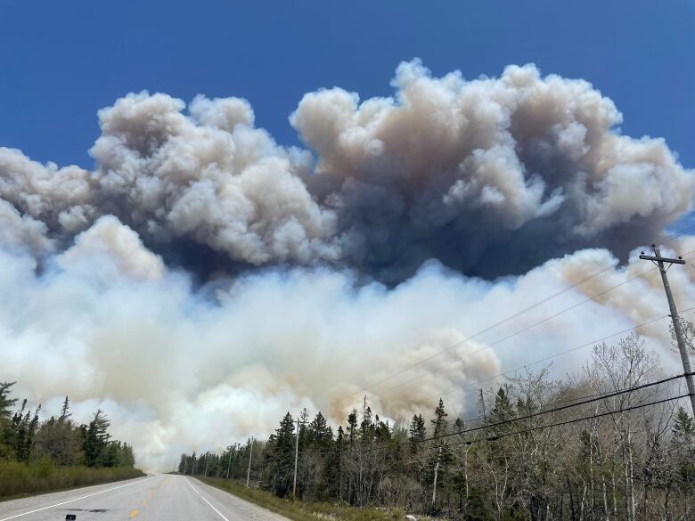 Billowing clouds of smoke from a wildfire are shown above a roadway.