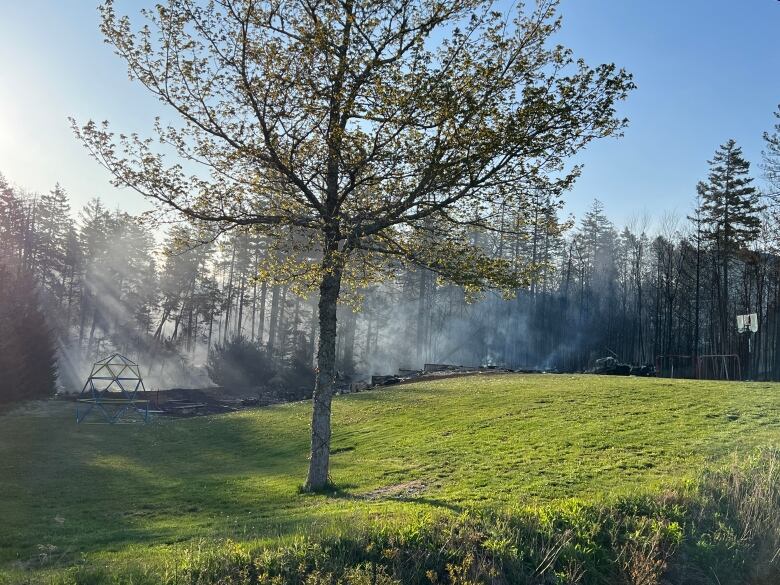 Smoke from a wildfire drifts upward near a singed area that contains children's playground with basketball hoop. 