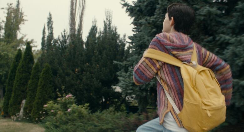 Still frame from the film Before I Change My Mind. Vaughan Murrae runs through trees while wearing a backpack.