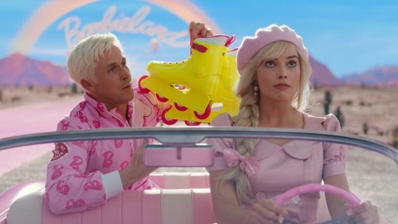 Still frame from the 2023 Barbie movie. Ryan Gosling as Ken and Margot Robbie as Barbie driving in a pink car. Ken eagerly holds up a yellow pair of rollerskates while Barbie rolls her eyes.