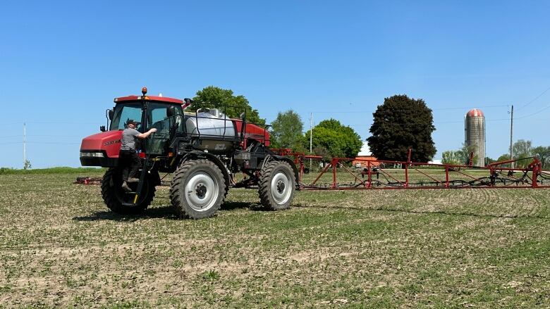 Farmer climbs up to the cab of his sprayer on a field of soybean.  