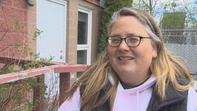 A woman with glasses speaks to the camera.