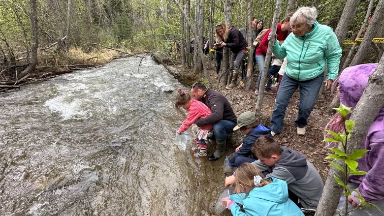 People crouch and stand on the bank of a stream.