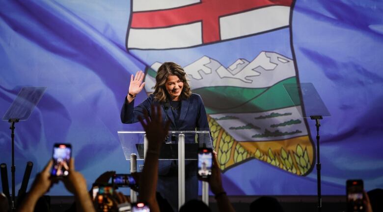 The Premier waves to a crowd from behind a podium.