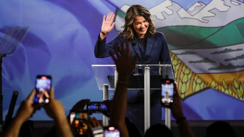 The Premier waves to a crowd from behind a podium.