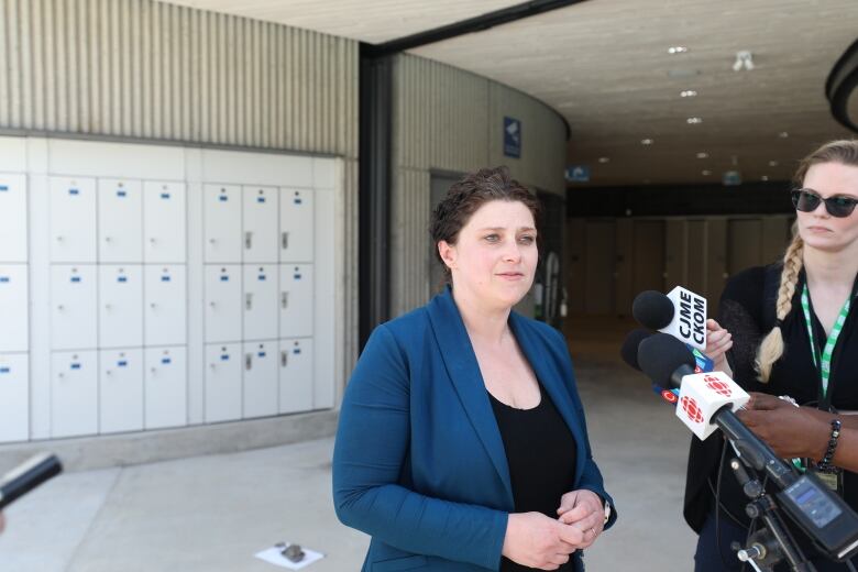 A woman wearing a black dress and a blue blazer speaks with media. 