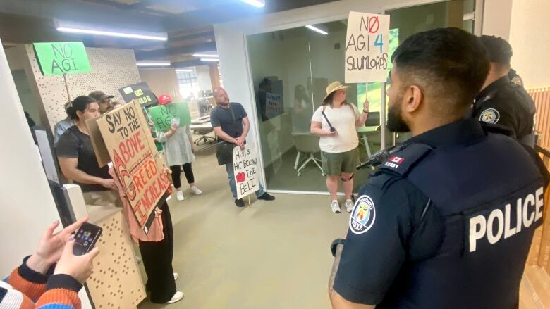 A group of residents holding placards while a police officer looks on.